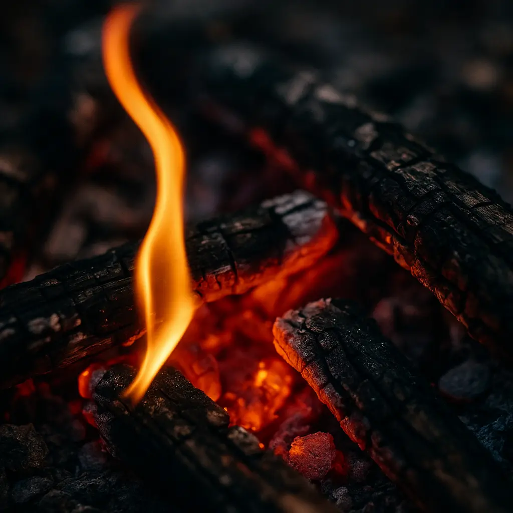 熾火の上で揺らめく小さな炎。黒く焼けた薪と赤く輝く炭が熱を放つ様子。