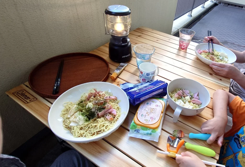 3人分の料理と飲み物が並ぶテーブル。ベランダの落ち着いた雰囲気の中で食事を楽しむ風景